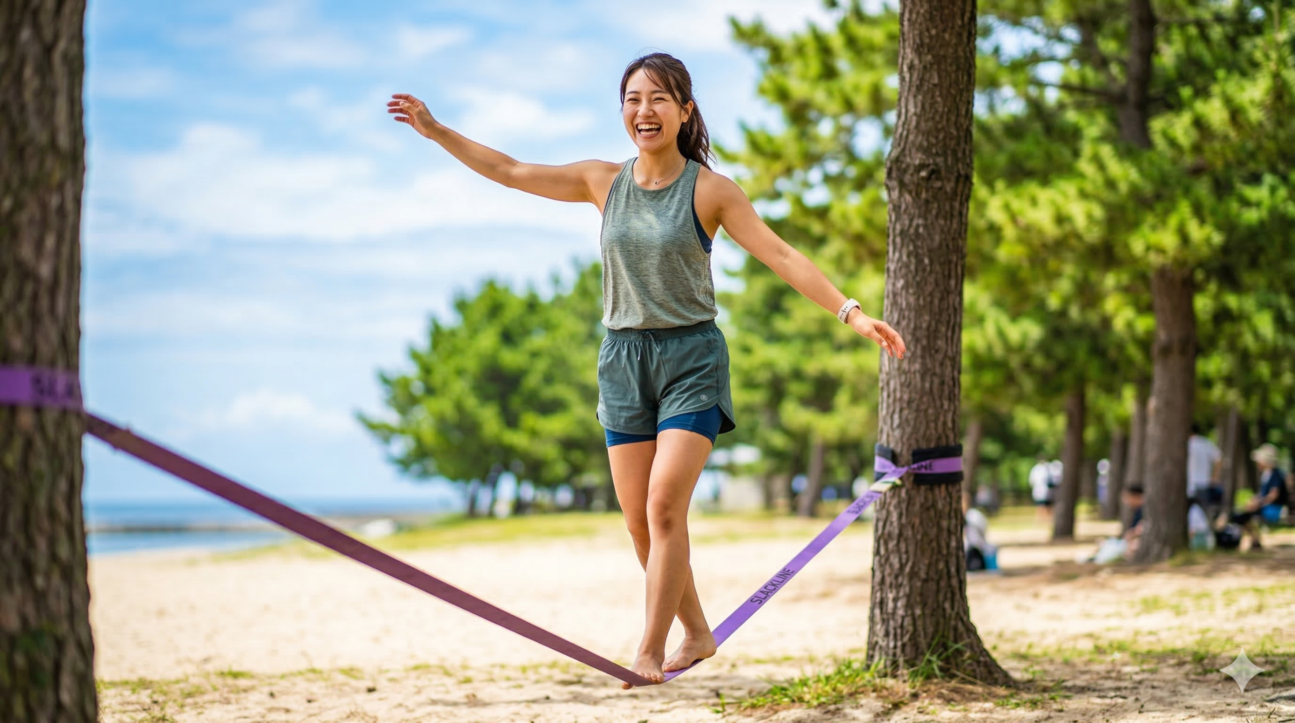 海岸沿いの公園にある木と木の間に張られた紫色のスラックラインの上を、素足でバランスを取りながら笑顔で歩く日本人女性
