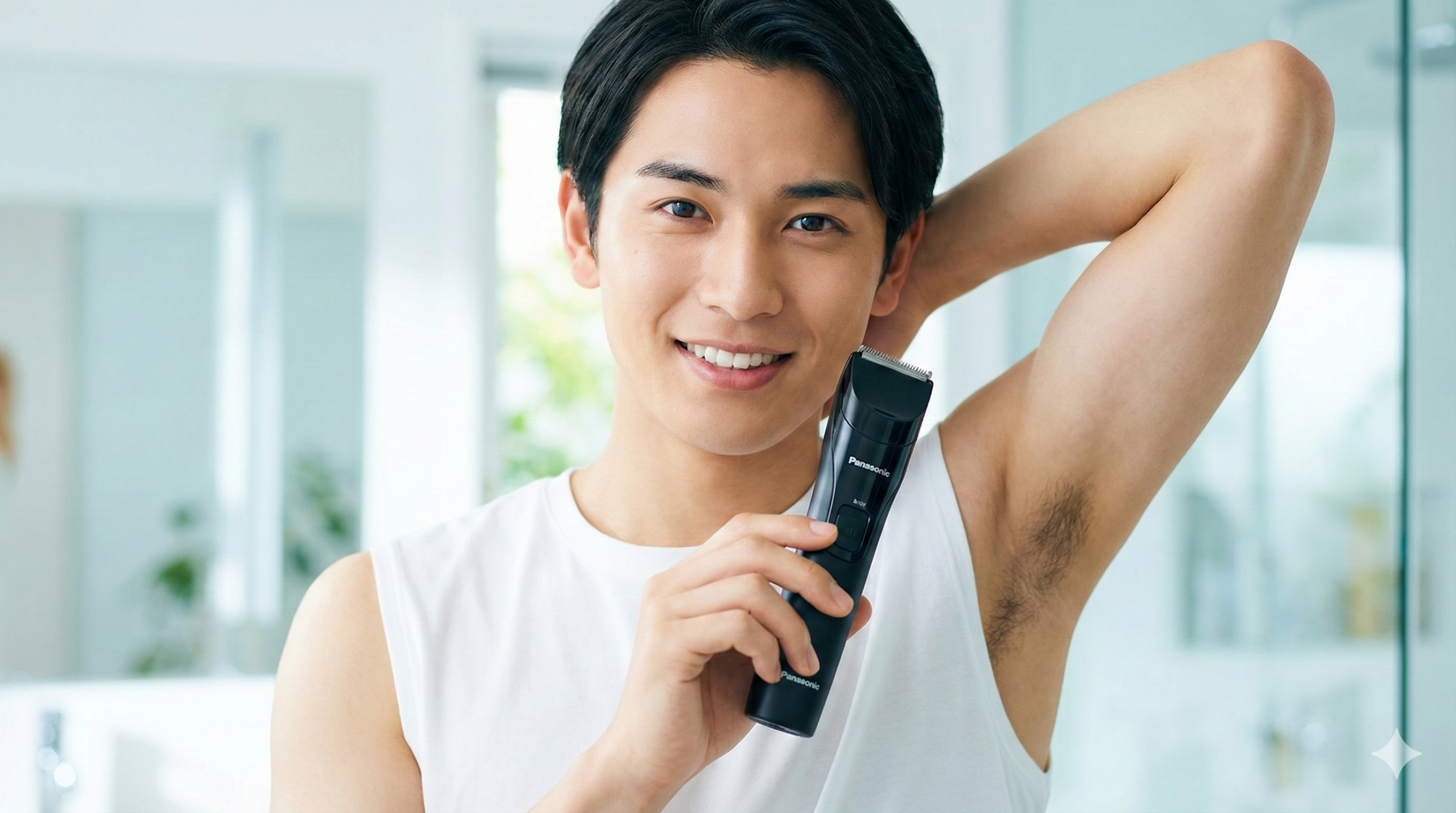 白いタンクトップを着て片腕を上げ、黒いボディトリマーを手に持ち爽やかに微笑む日本人男性